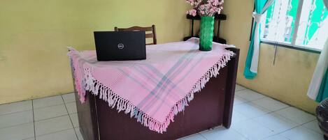 A desk with a laptop, a vase with flowers, and a table covered with a plaid tablecloth.