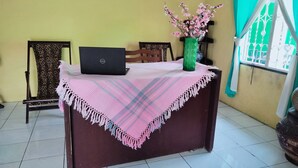 Una habitación con escritorio, laptop, un jarrón con flores y ventana con vistas.