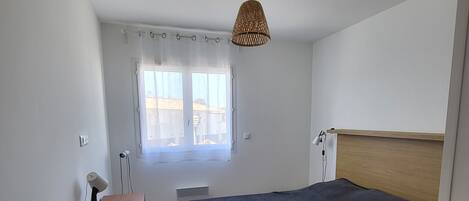 A bedroom with a bed, a desk with a lamp, a window with curtains, and a ceiling fan.