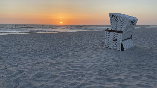 A beach chair with a number on it, positioned on a sandy beach with the ocean and a sunset in the background. - Die Wohnung Treibholz mit Balkon Liegt in Einer Sehr Ruhigen Lage in Hörnum (Hörnum (Sylt))