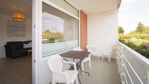 A balcony with a table and chairs, a sofa inside, and a view of greenery and trees. - Die Wohnung Treibholz mit Balkon Liegt in Einer Sehr Ruhigen Lage in Hörnum (Hörnum (Sylt))
