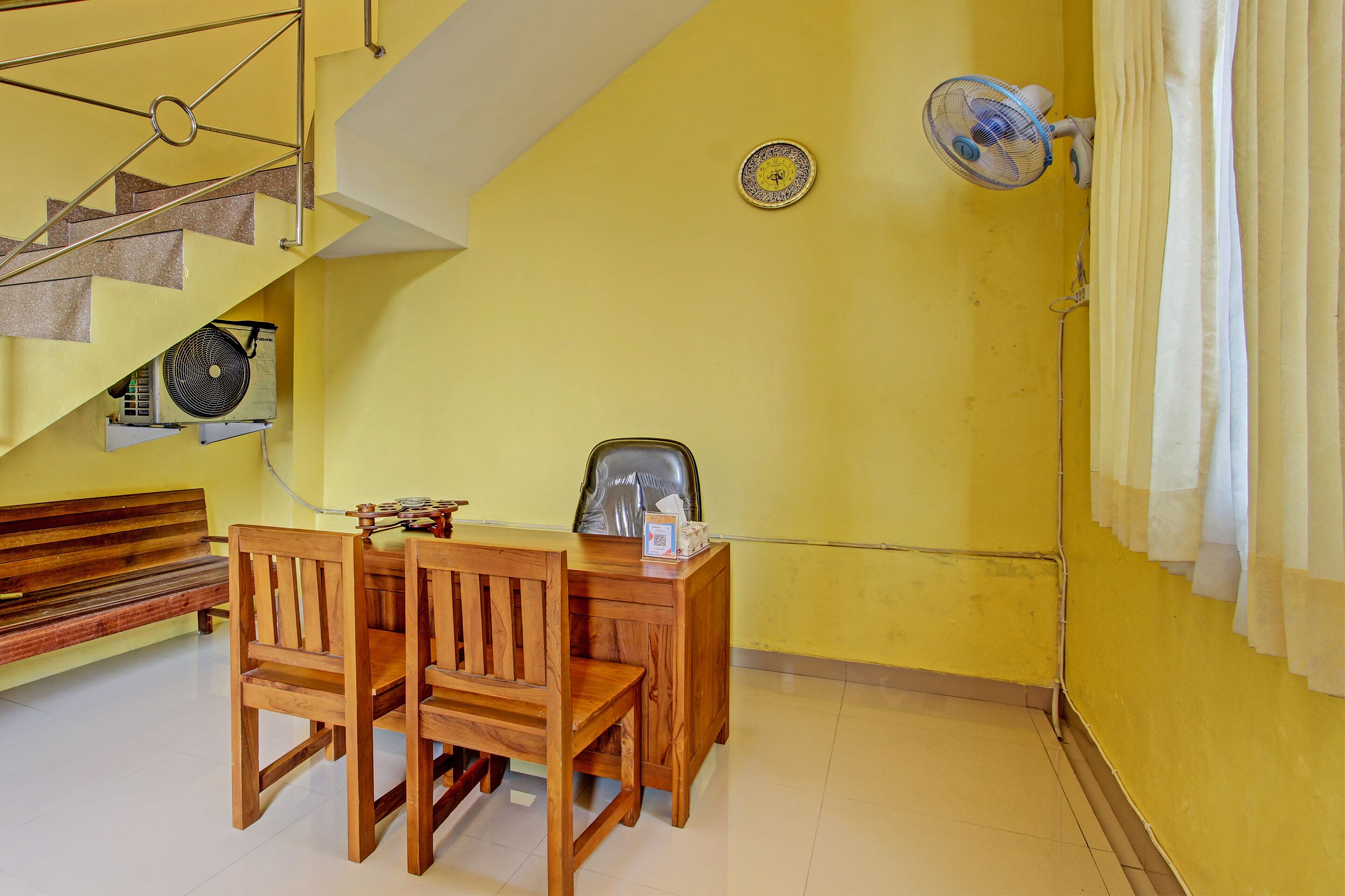 A room with a wooden dining table and chairs, a bench, a ceiling fan, and a staircase with a decorative railing.