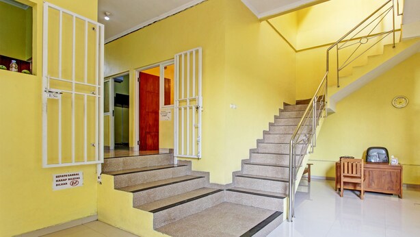 A staircase with a handrail, a wooden desk, and a chair in a room with yellow walls. - Hotel O Umi Rahayu Guesthouse (Semarang)