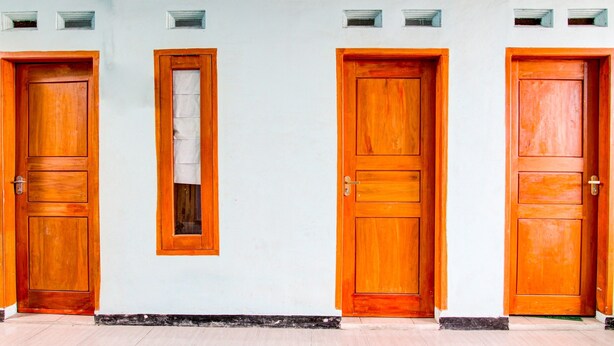 A row of three wooden doors with a white wall and small windows above them. - Hotel O Gioba Kost Syariah (Wirosari)