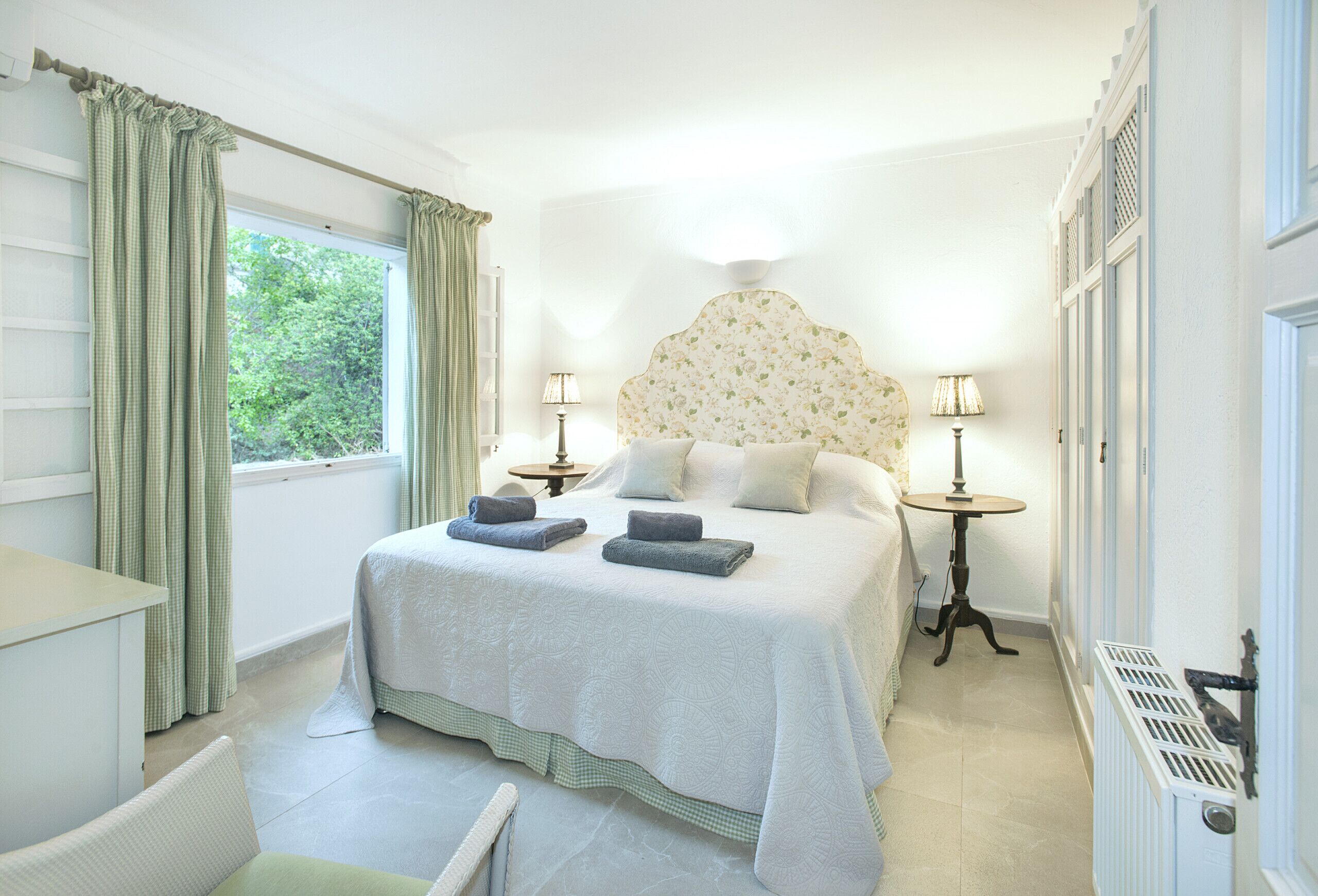Quarto bem arrumado com uma cama grande, duas mesas de cabeceira com luminárias, uma janela com cortinas e um radiador.