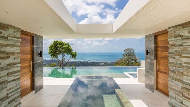 Un interior moderno con un amplio techo de vidrio, vista al océano y un área de piscina.