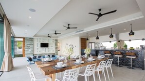 Un comedor moderno con una mesa de madera larga, sillas blancas y ventiladores de techo.