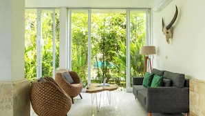 A modern living room with a sofa, two wicker chairs, a coffee table, and a large window offering a view of lush greenery. - Casa Sweet Lips by Betterplace (Canggu)
