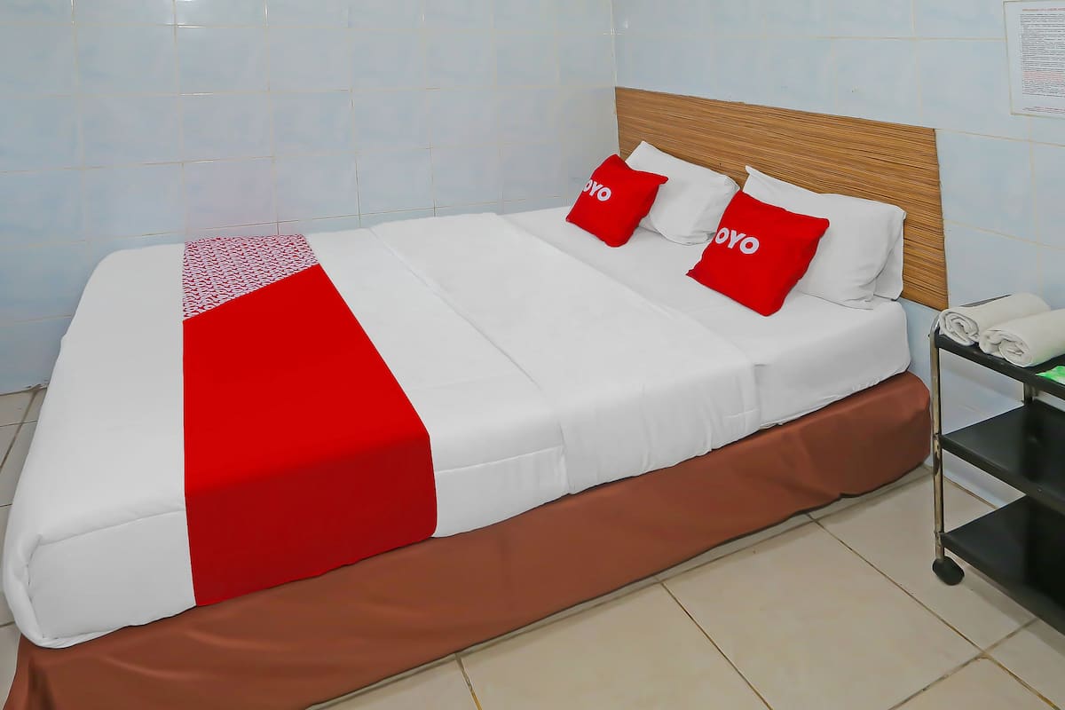 Ein ordentlich bezogenes Bett mit einer roten und weißen Tagesdecke, zwei rote Kissen mit dem Schriftzug "YOYO" und ein brauner Bettvorhang.