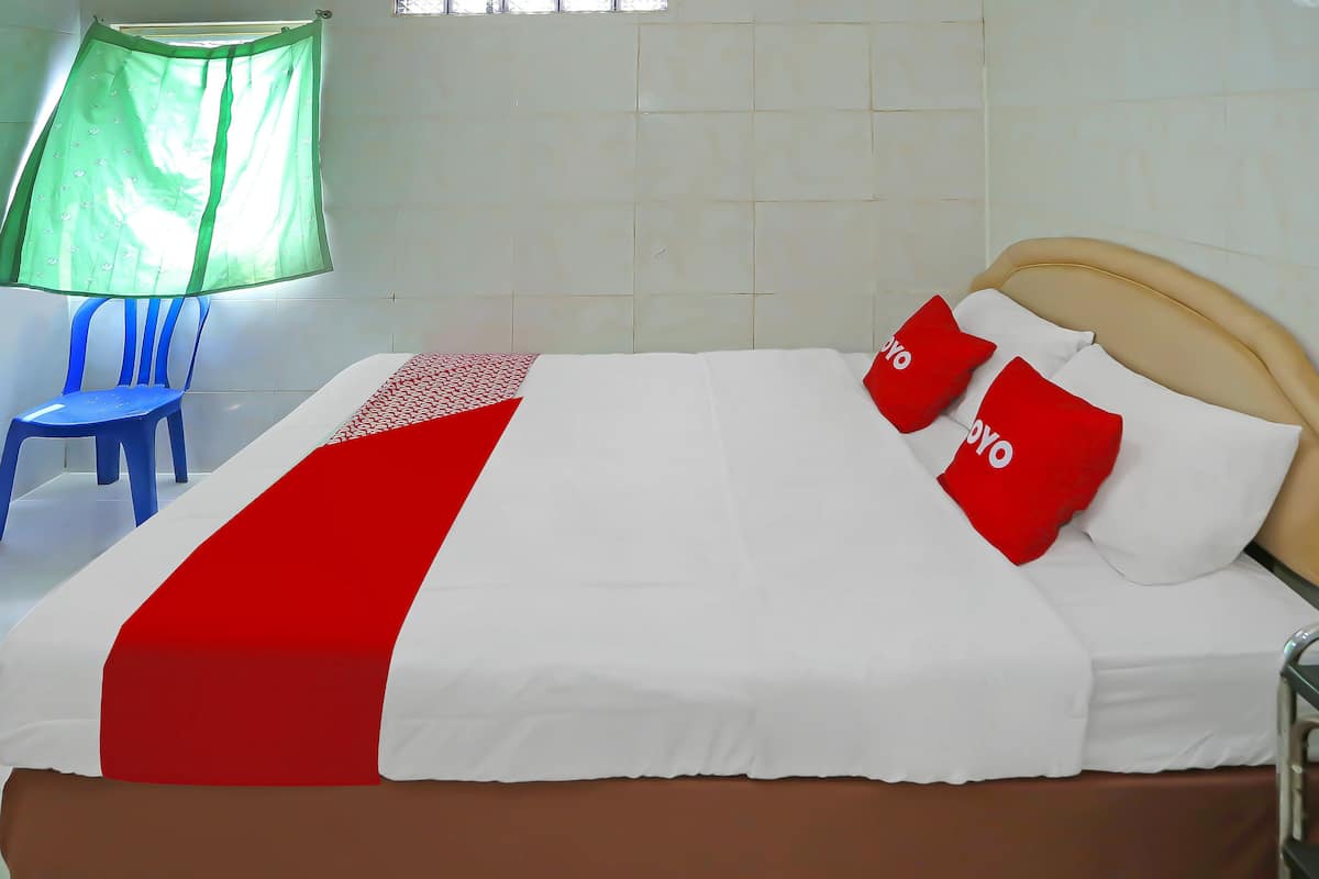 Ein Bett mit einer roten und weißen Tagesdecke, zwei rote Kissen und ein braunes Kopfteil.