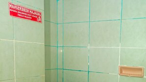 Une petite salle de bain simple, avec des toilettes, des murs recouverts de carreaux verts et un panneau rouge indiquant les consignes de sécurité.