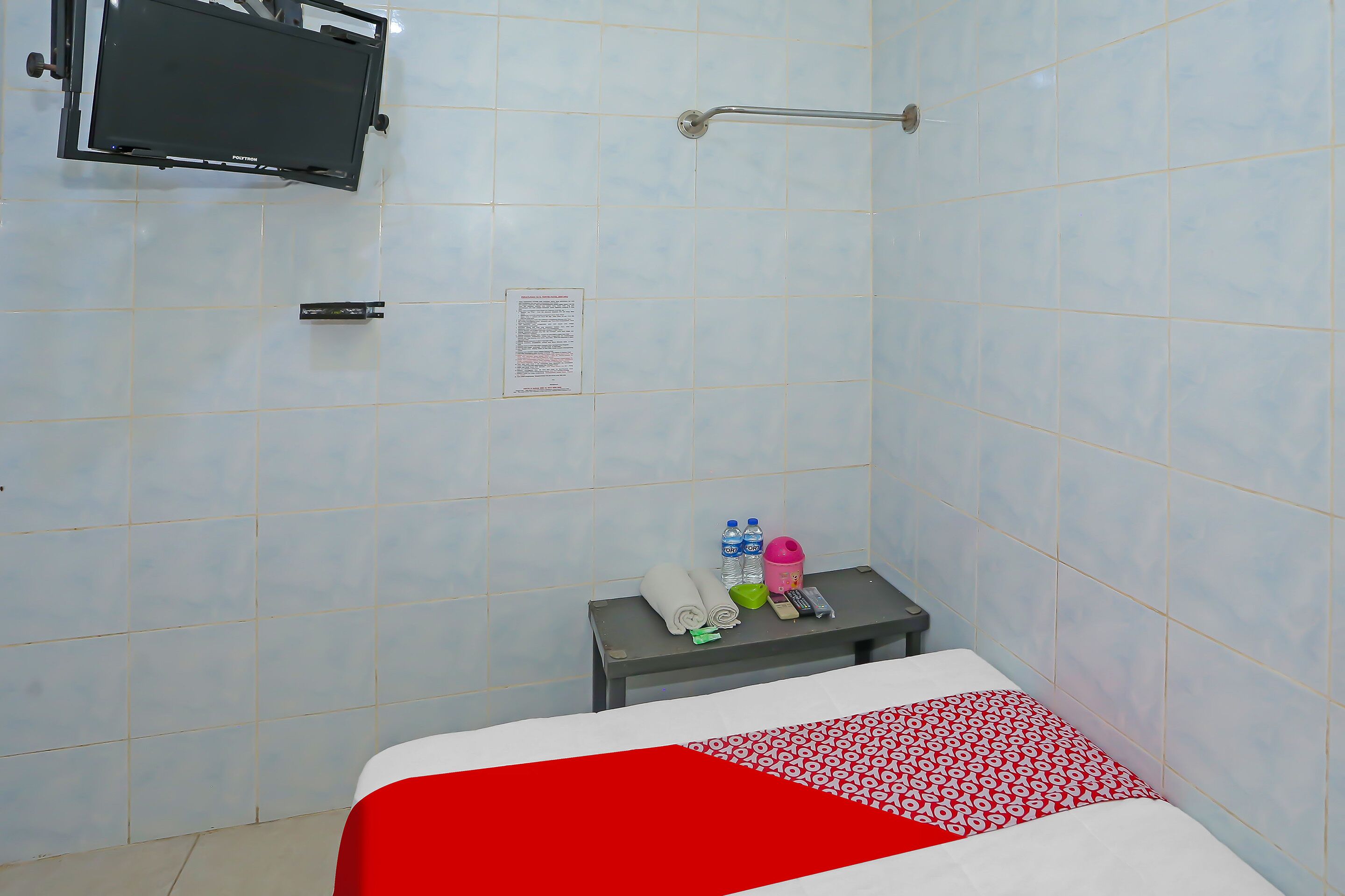 Hotelkamer met een bed, een klein tafeltje met toiletartikelen, een aan de muur bevestigde televisie en een douche.