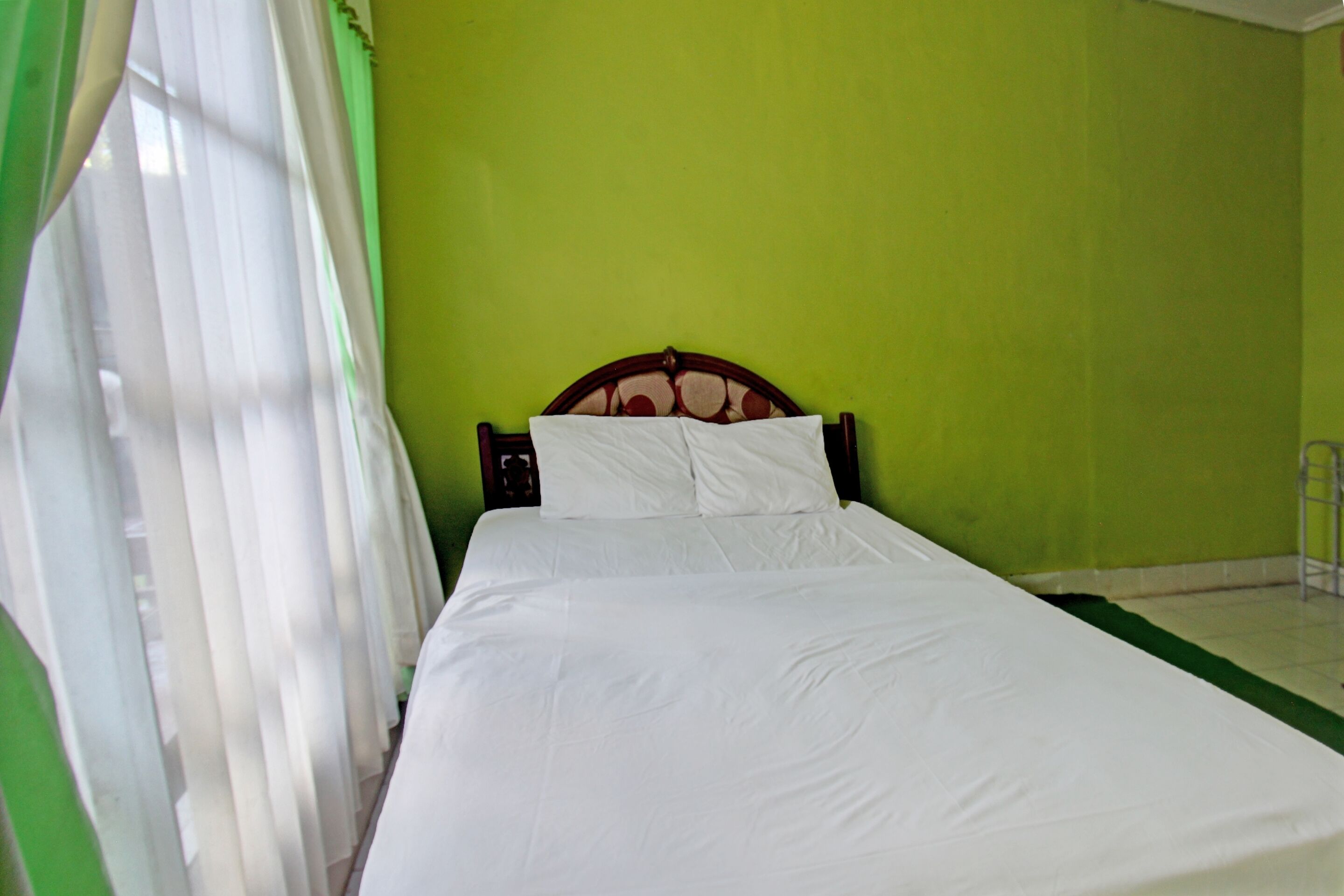 A bed in a room with green walls and white curtains.