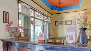 Een receptiebalie met een bord waarop ‘RECEPTIONIST’ staat, een ingelijst certificaat en een vaas met bloemen.