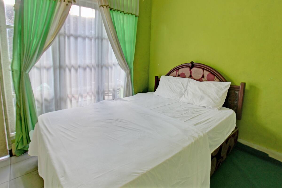 Een net opgemaakt bed in een kamer met groene wanden en een raam met groene gordijnen.