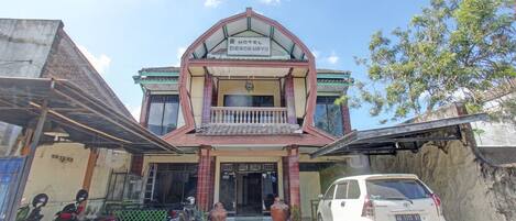 A hotel with a traditional architectural style, featuring a prominent entrance with a tiled roof and a balcony.