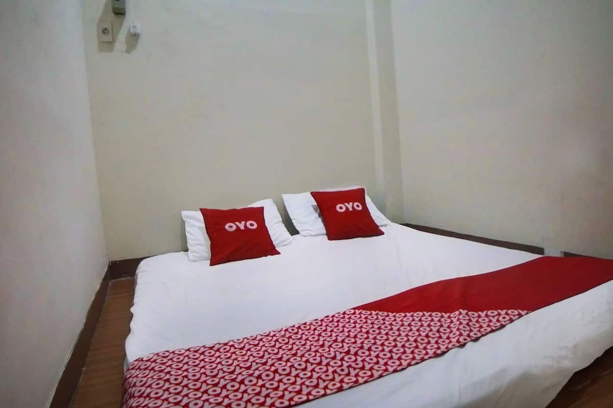 Ein ordentlich bezogenes Bett mit einer Bettdecke in Weiß und Rot und zwei Kissen mit dem Schriftzug 'OYO'.