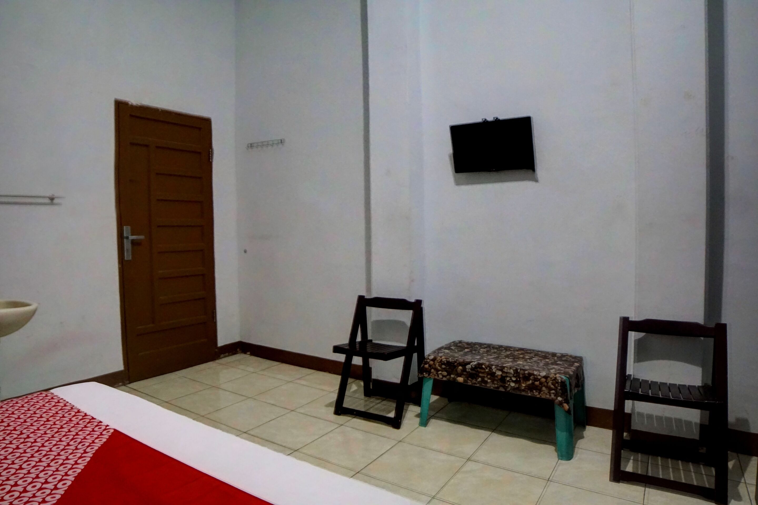 Una habitación con una cama, dos sillas, una mesita, un televisor y una puerta.