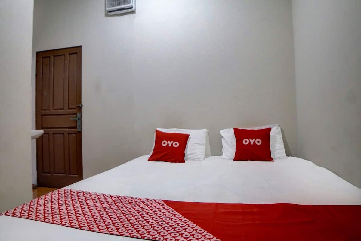 Ein Hotelzimmer mit einem Bett, zwei Kissen mit dem Schriftzug "OYO", einer rot-weißen Decke und einer Holztür.