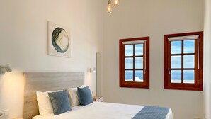 Een slaapkamer met een bed, twee ramen, een nachtkastje, een wandlamp en een schilderij.