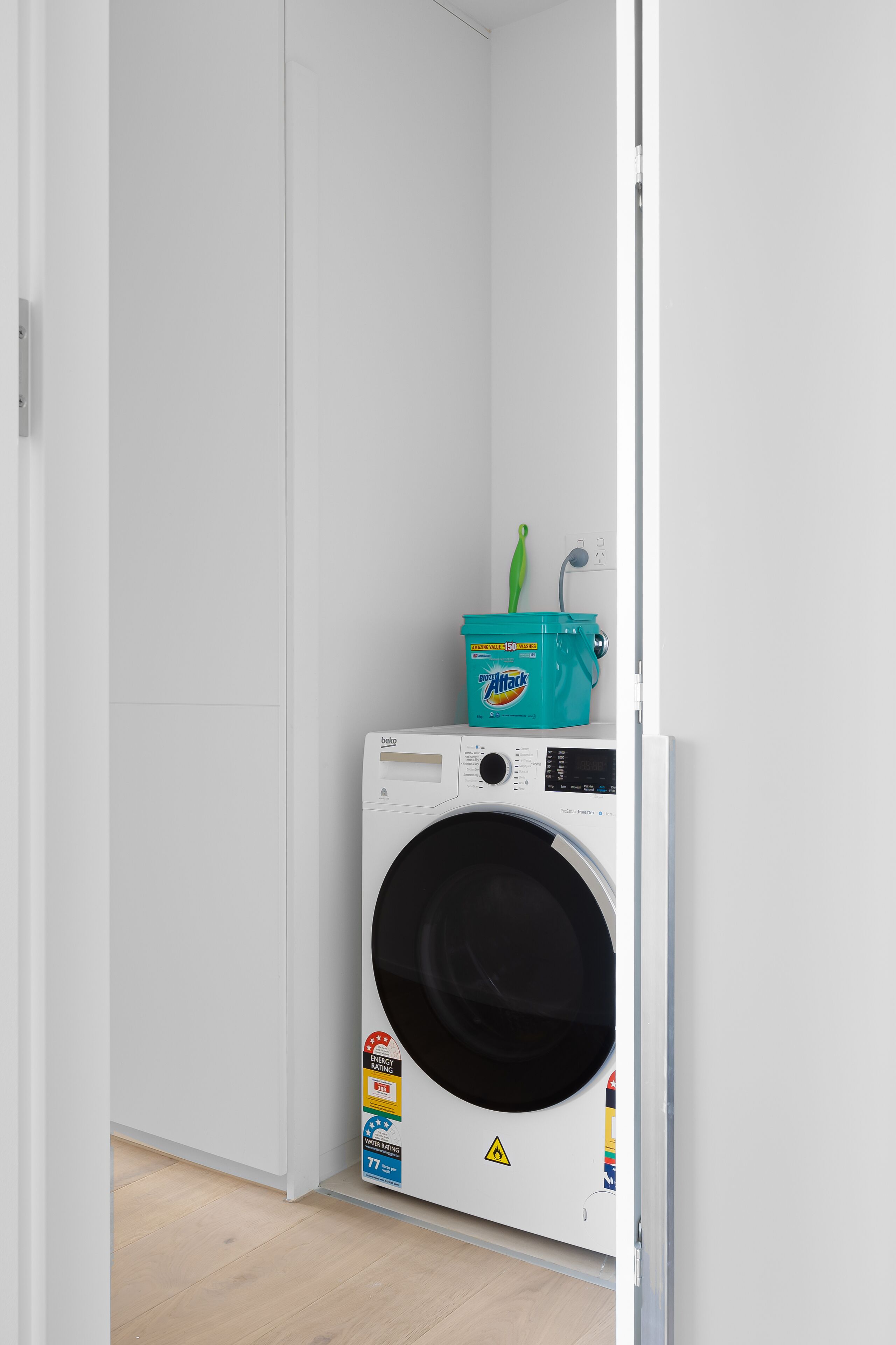 A compact laundry room with a front-loading washing machine, a green bucket, and a wall-mounted heater.