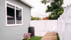 Un jardin avec une terrasse en bois, une clôture blanche et une maison grise.