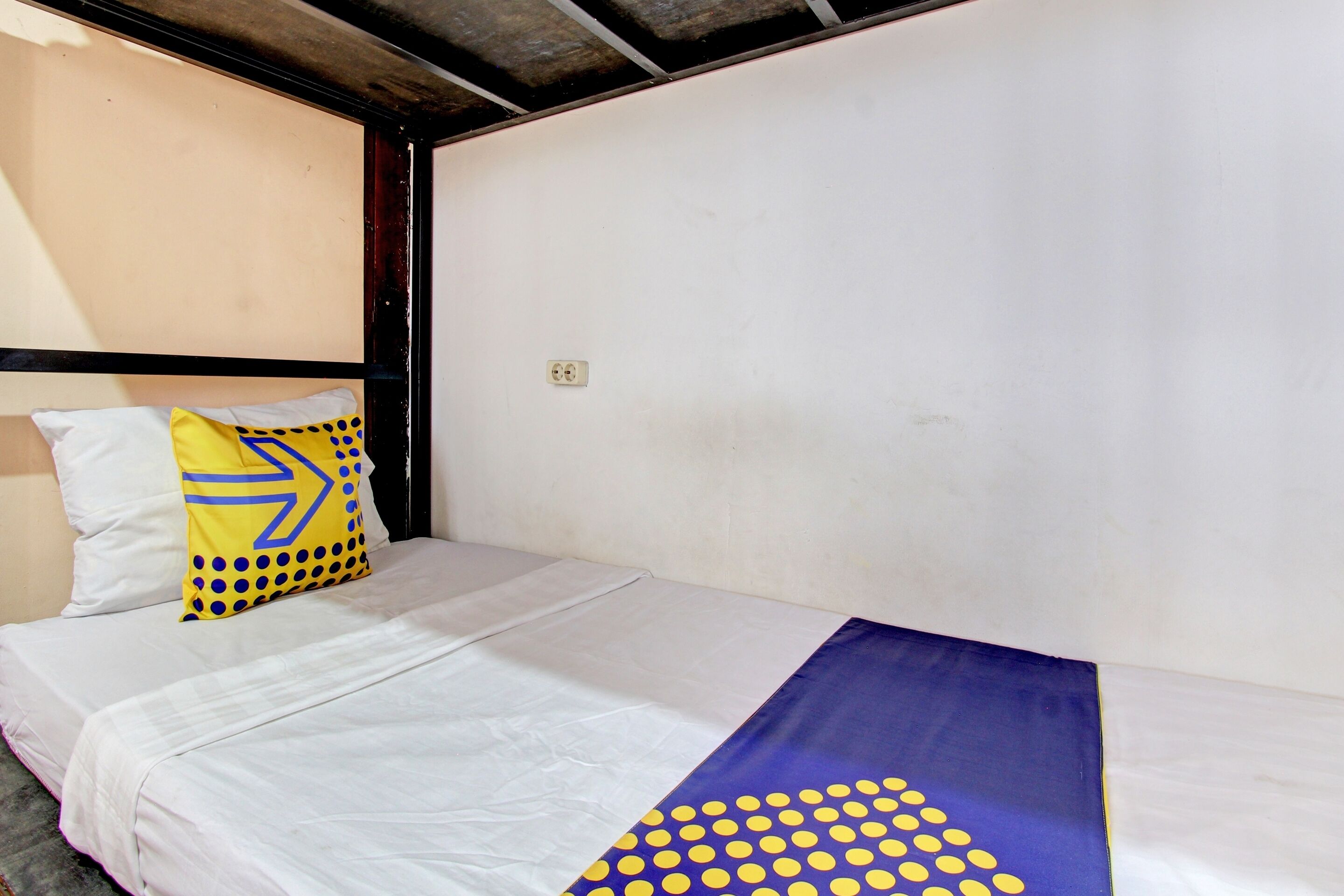 A single bed with white bedding and a blue and yellow patterned blanket.