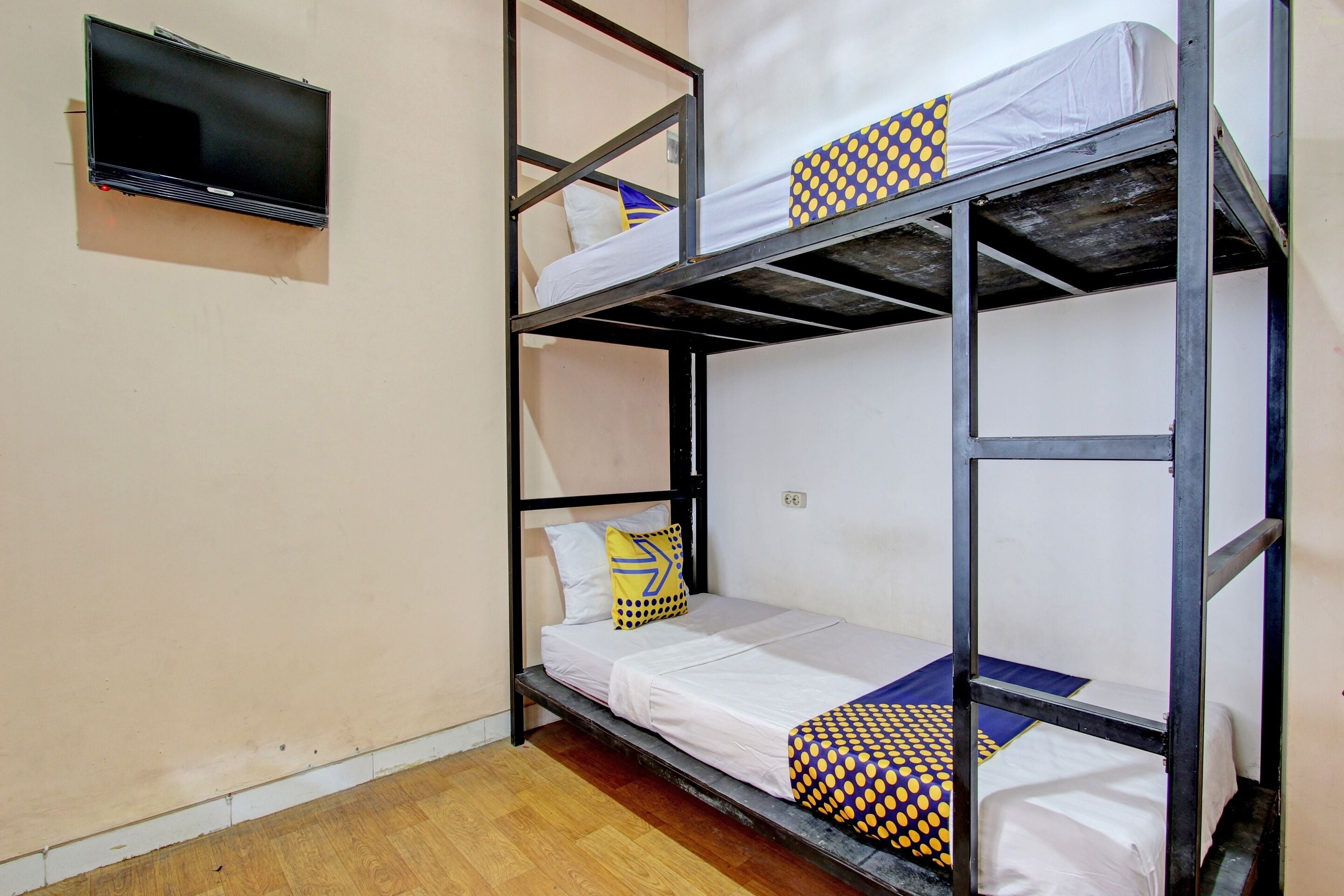 A bunk bed room with a television mounted on the wall, wooden flooring, and a simple, functional design.