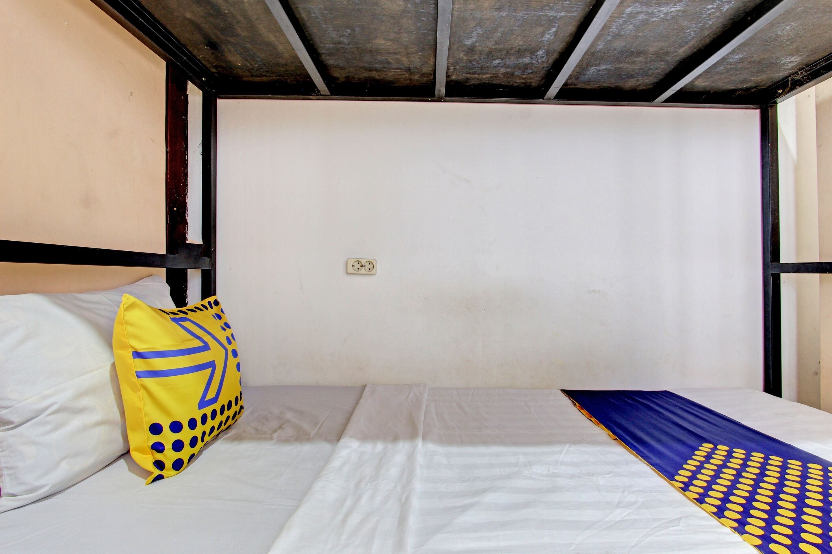 A single bed with a white mattress and a blue and yellow patterned blanket.