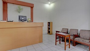 Un espace d’accueil comprenant un comptoir en bois, un écran d’ordinateur, un ventilateur et un coin salon avec deux canapés et une table.