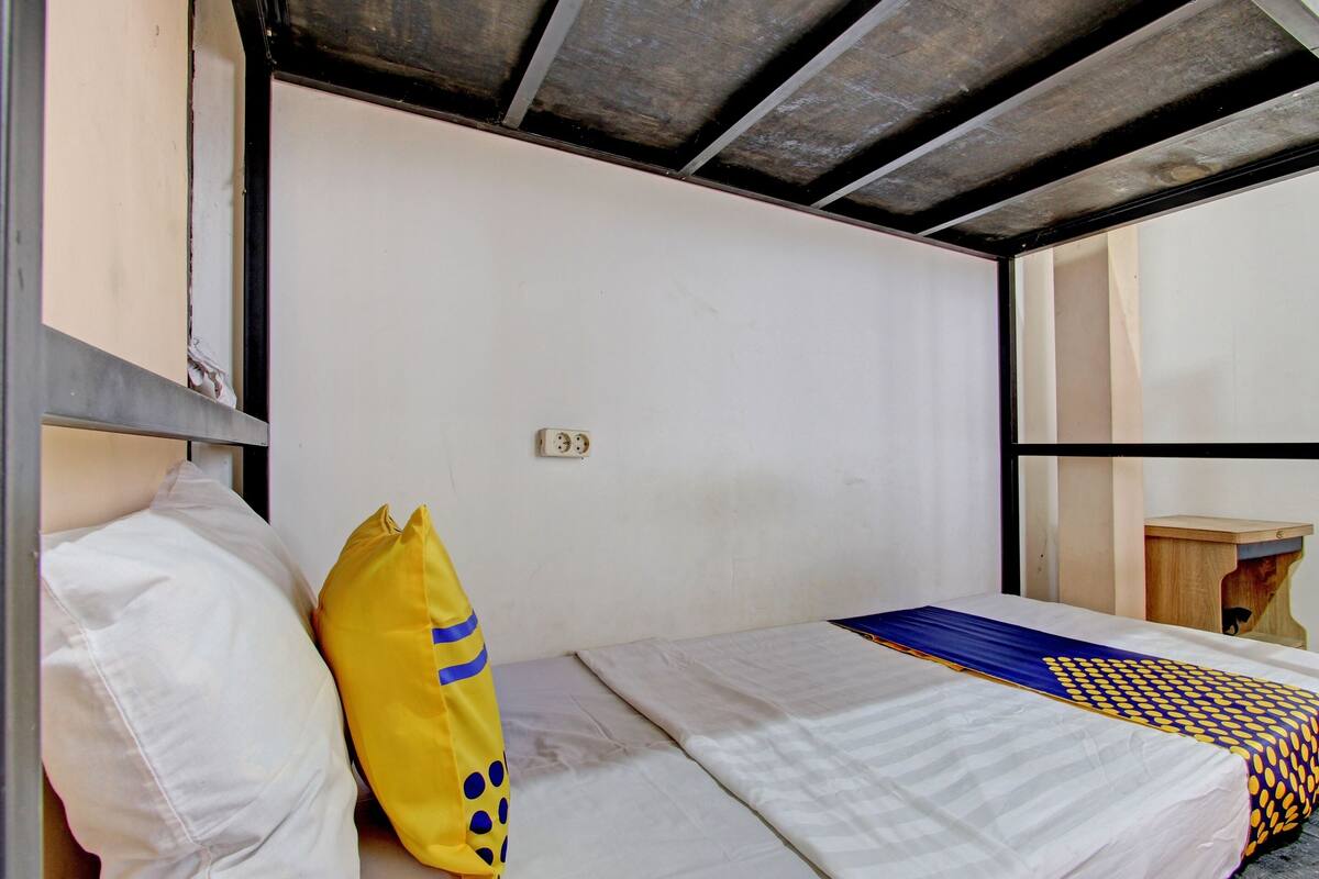 A single bed with a white mattress, a yellow pillow with blue patterns, and a blue and yellow patterned bedspread.