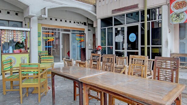 Un espace extérieur aménagé avec des tables et des chaises en bois, un stand de restauration et l’entrée d’un restaurant.