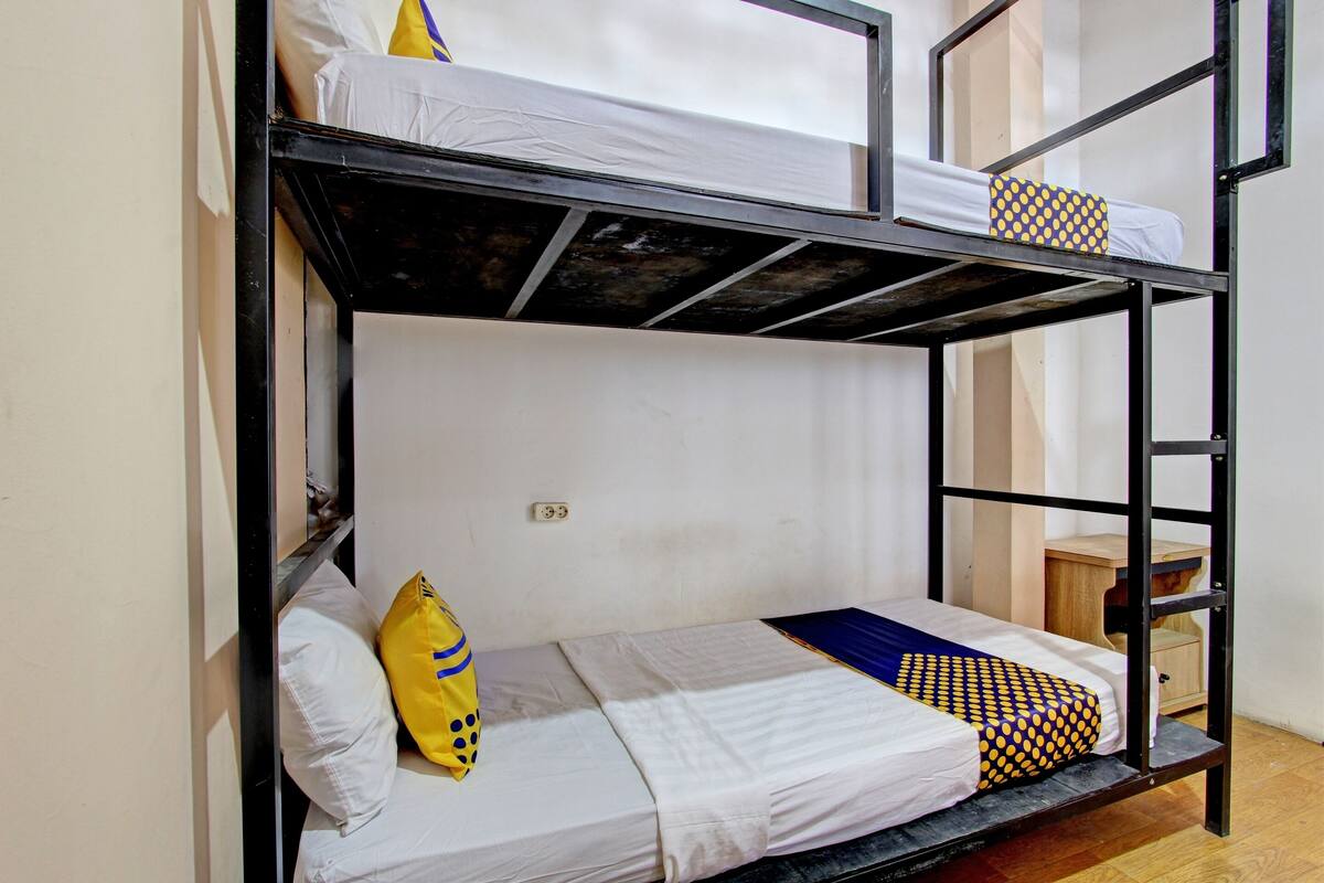 A bunk bed with a white mattress, a yellow pillow, and a blue and yellow polka dot pillow.