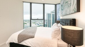 A bedroom with a large window, a bed with white linens, a dark headboard, and a modern lamp. - Panoramic Paradise , Parking & Amenities (Southbank)