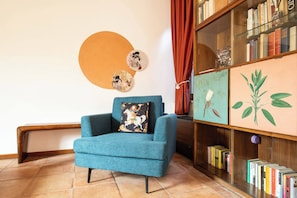 Ein Zimmer mit einem blaugrünen Sessel, einem Bücherregal mit Büchern und dekorativer Wandkunst.