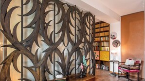 A room with a decorative metal partition, a wooden cabinet with books, a small table with a lamp, and a bookshelf. - Dimora Del Filosofo (Verona)