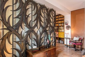 Una stanza con un pannello decorativo in metallo, un armadietto in legno con libri, un tavolino con una lampada e una libreria.