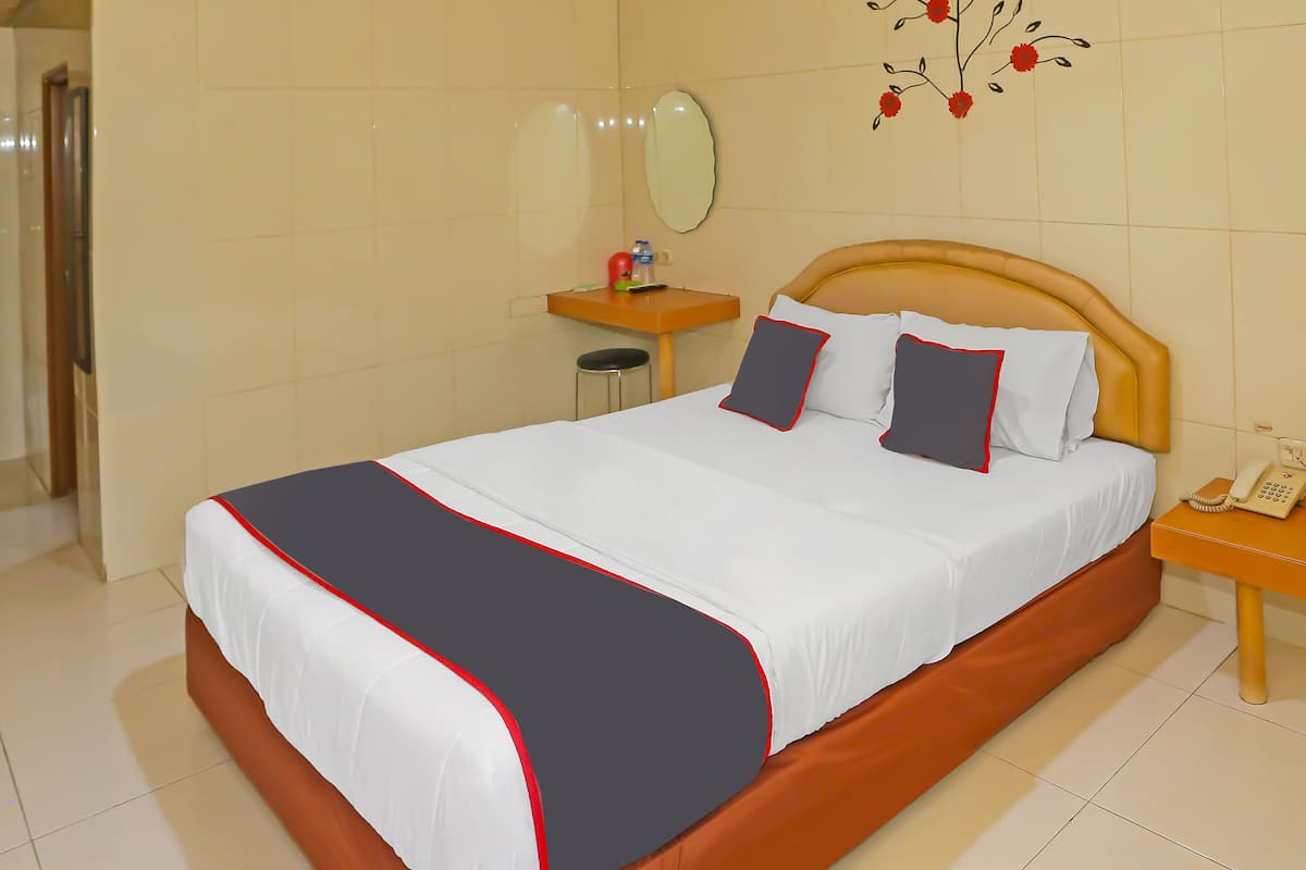 A hotel room with a bed, a bedside table with a phone, a small stool, and a wall-mounted mirror.