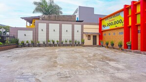 A hotel with a large parking area, multiple garage doors, and a promotional sign advertising a Rp. 200,000,000 holiday package. - Hotel O Sion Holiday (South Tangerang)