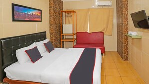 A hotel room with a bed, a TV, a red chair, a shelf with a remote, and a painting on the wall. - Hotel O Sion Holiday (South Tangerang)