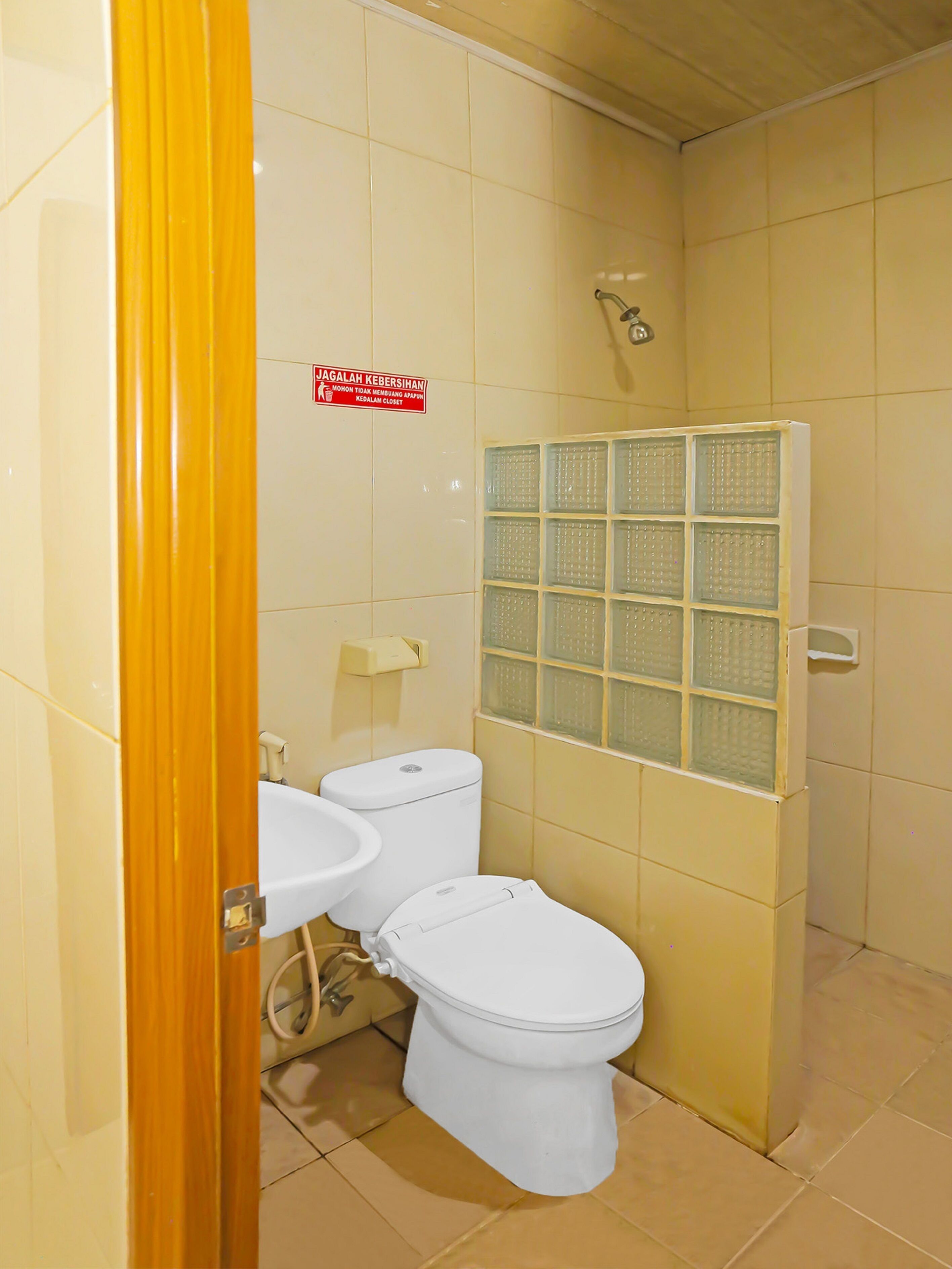 A bathroom with a toilet, sink, and shower. There is a sign on the wall and a window with a grid pattern.