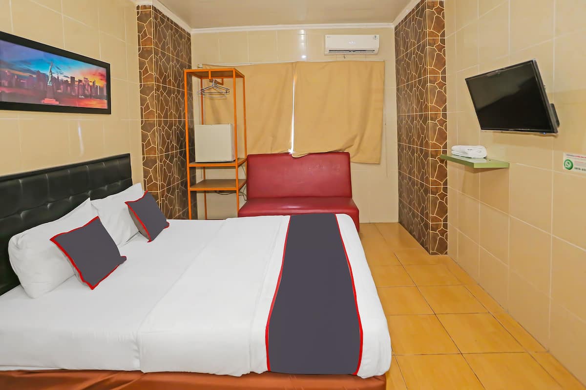 A hotel room with a bed, a TV, an air conditioner, a towel rack, and a cityscape painting.