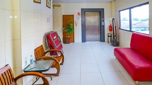 A hotel lobby with a red sofa, wooden chairs, a small table, a potted plant, an elevator, and a window with a view. - Hotel O Sion Holiday (South Tangerang)