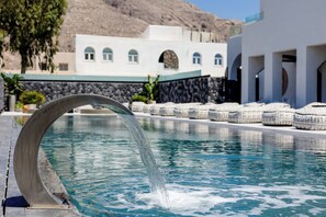 A pool with a modern water feature, a stone wall, and a building with arched windows in the background. - Santo Mangata Boutique Hotel & Spa - Adults Only (Santorini)