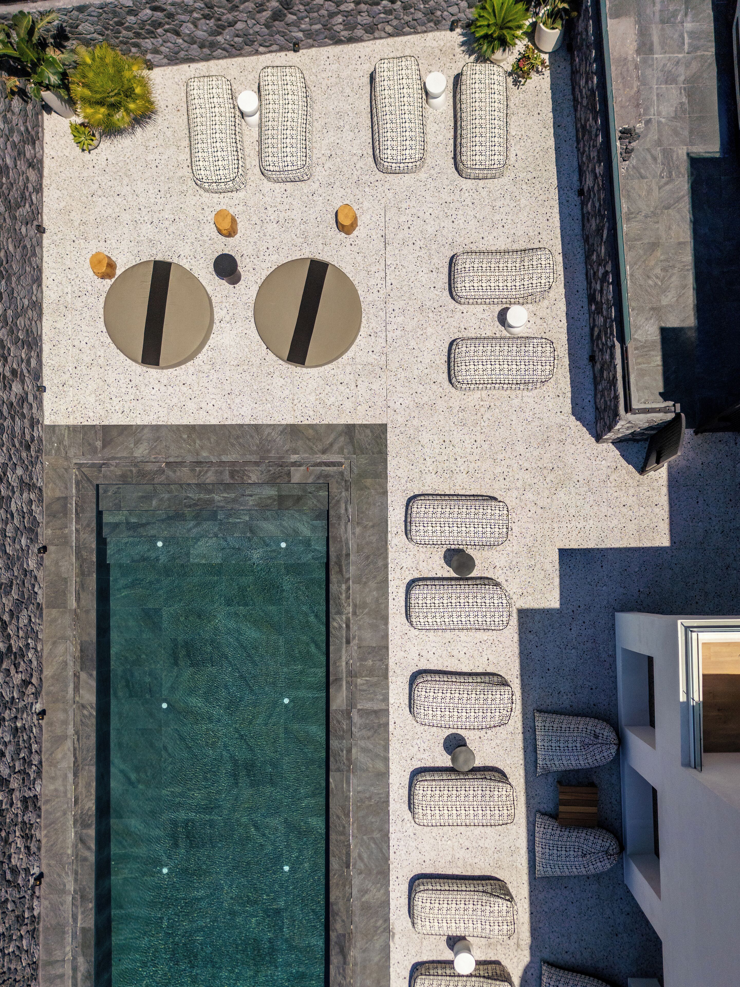 Vue aérienne d’un espace aménagé autour d’une piscine, avec des chaises longues, une petite piscine et un mur en pierre.