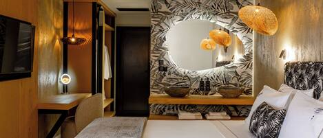 A modern hotel room with a large bed, a wooden desk, a mirror with a circular frame, and a wall with a leaf pattern.