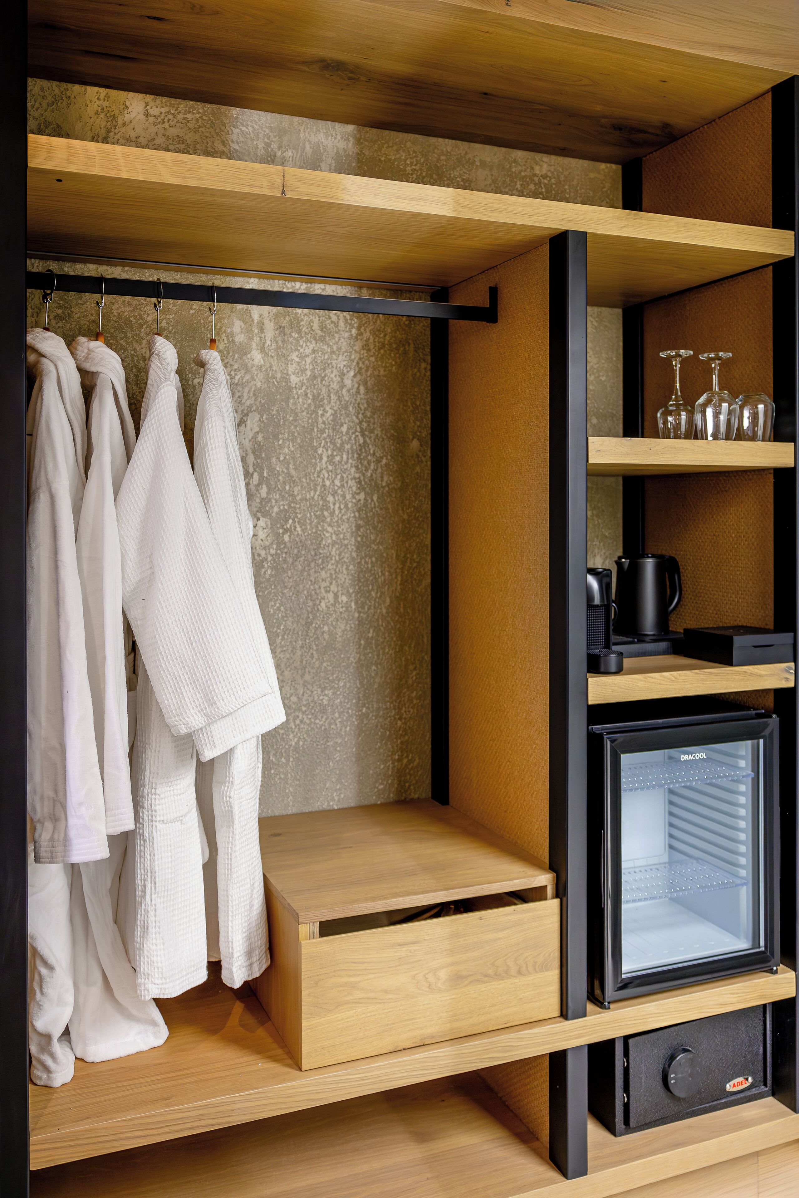A compact storage unit with hanging robes, a coffee maker, and a mini-fridge.