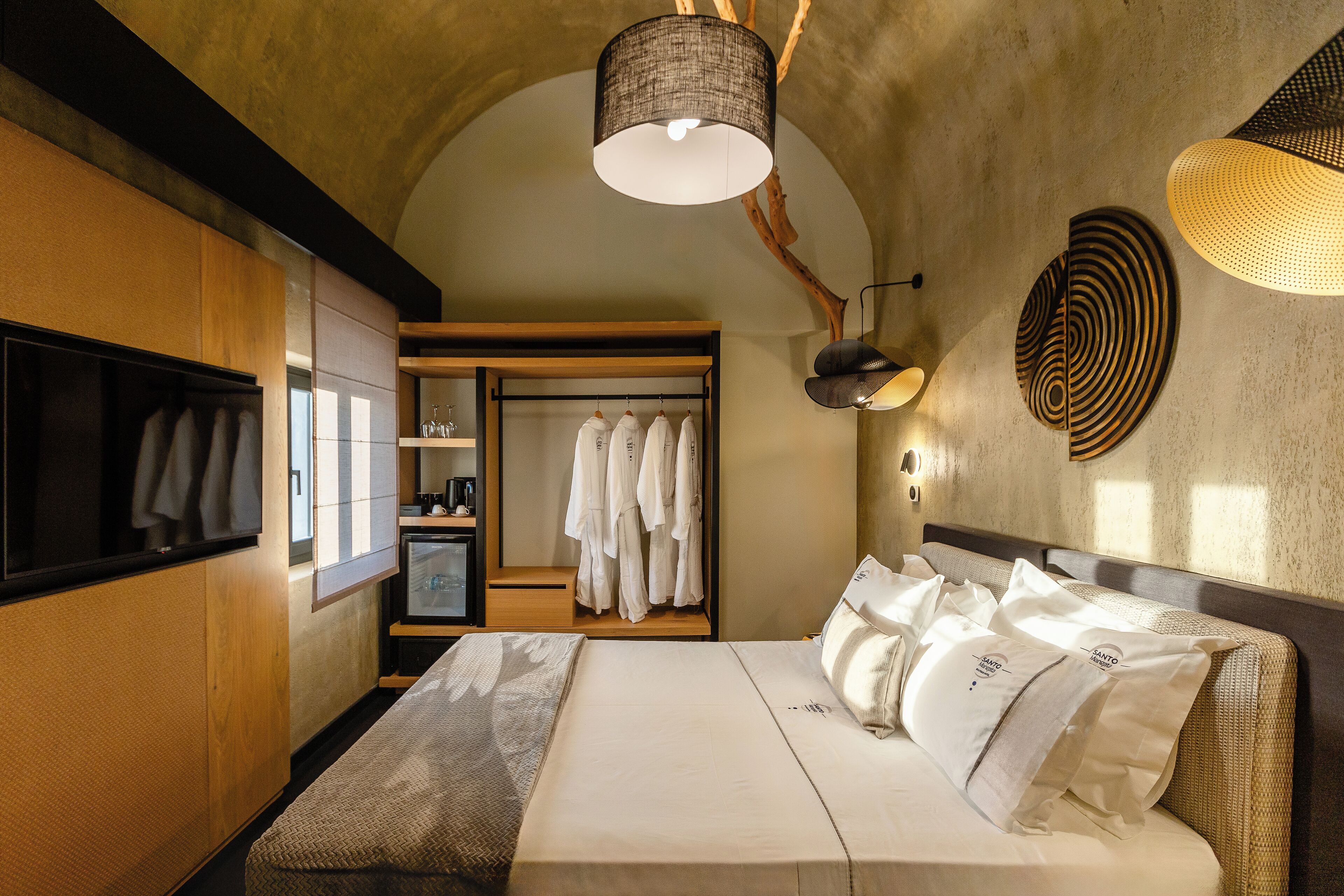 A bedroom with a large bed, a wardrobe, a mirror, and a closet with hanging clothes.
