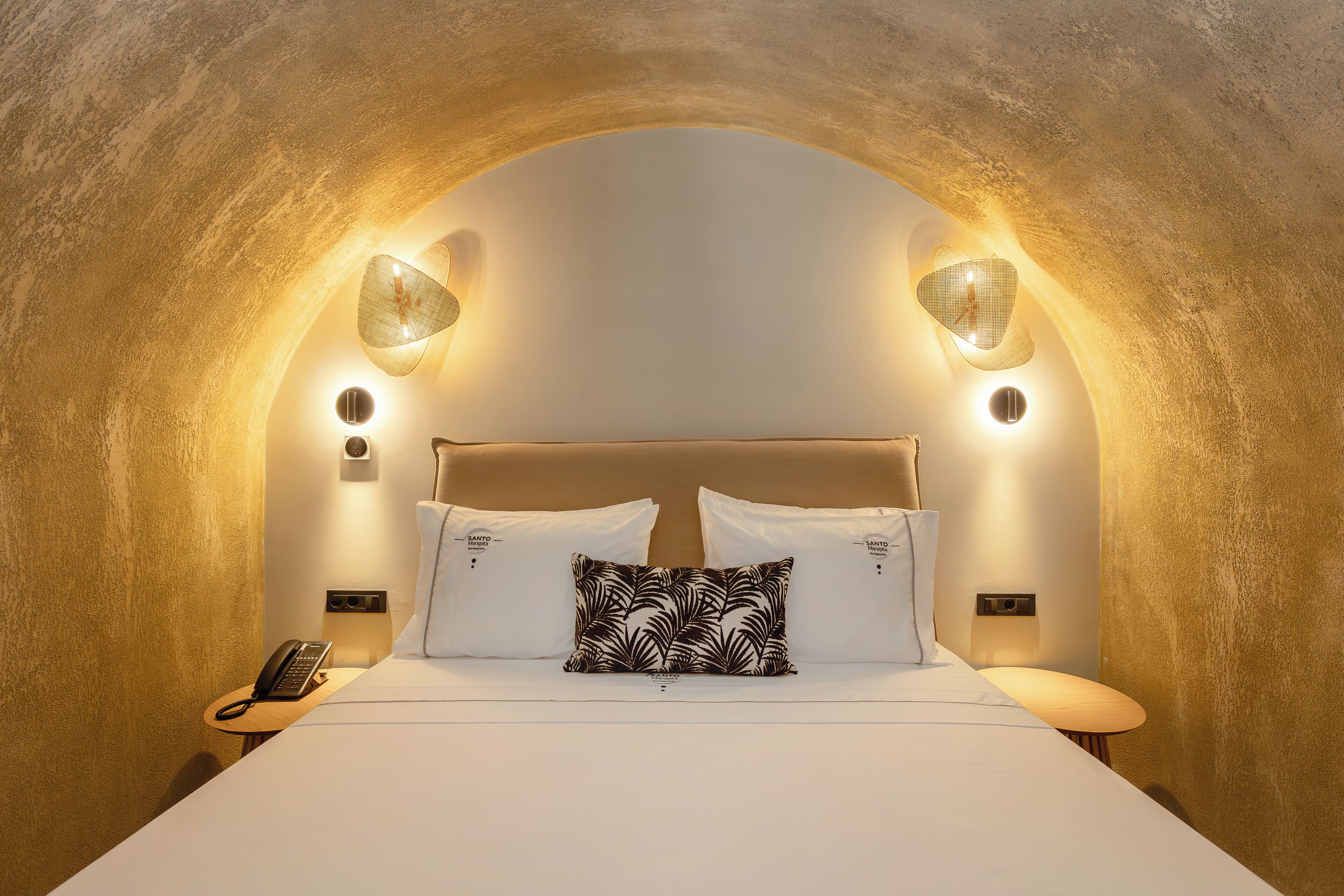 A bedroom with a vaulted ceiling, a bed with white linens, a patterned pillow, and wall-mounted lamps.