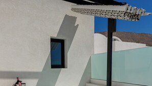 Un jacuzzi moderno al aire libre con barandilla de vidrio, una ventana pequeña y un cuenco con fruta y un vaso de agua.